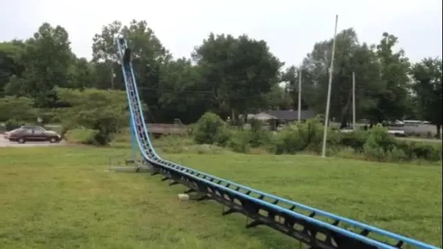 A hand-drawn ink illustration of a small backyard roller coaster track curving through a grassy field